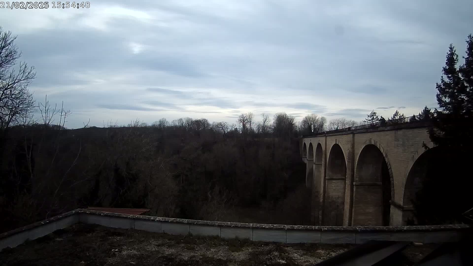 A stone arched viaduct stretches across a wooded valley under a cloudy sky.