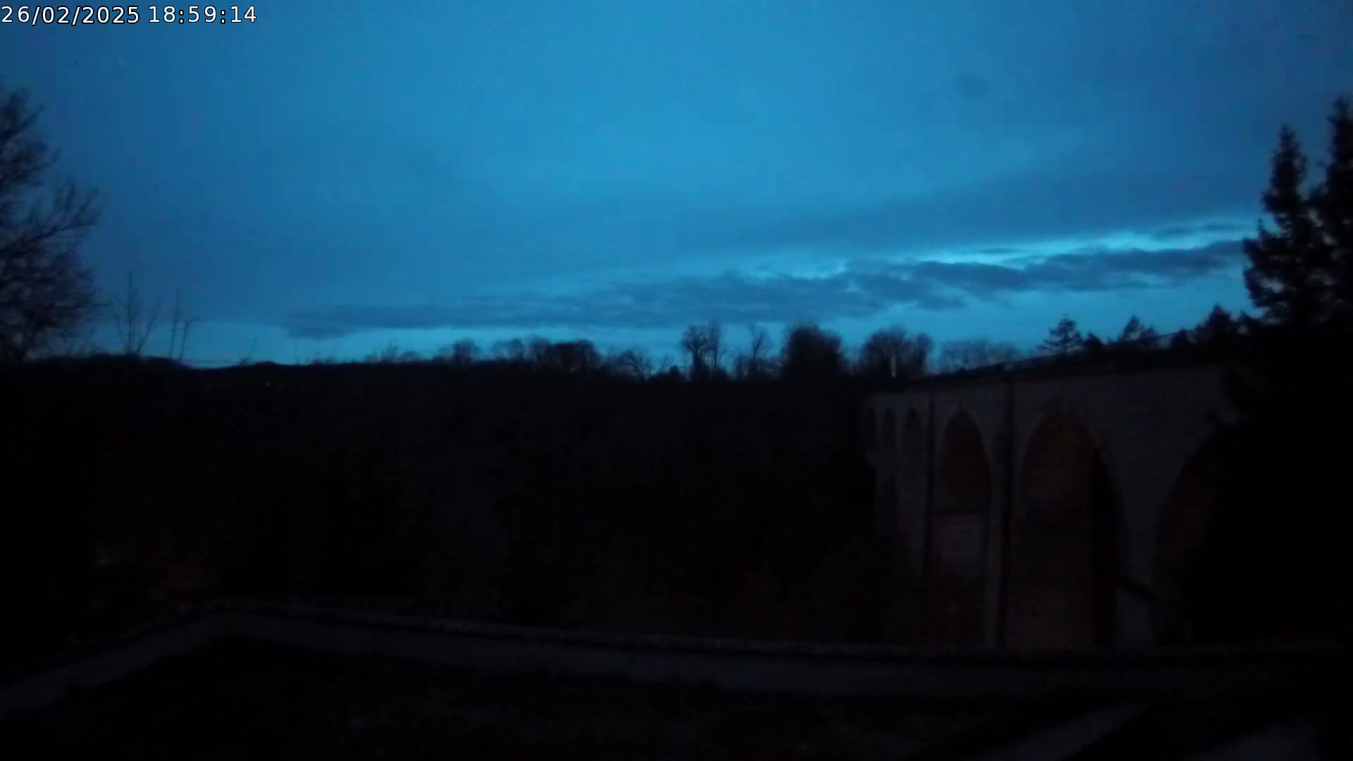 A dark, silhouetted stone bridge is visible against a twilight sky with thin clouds.