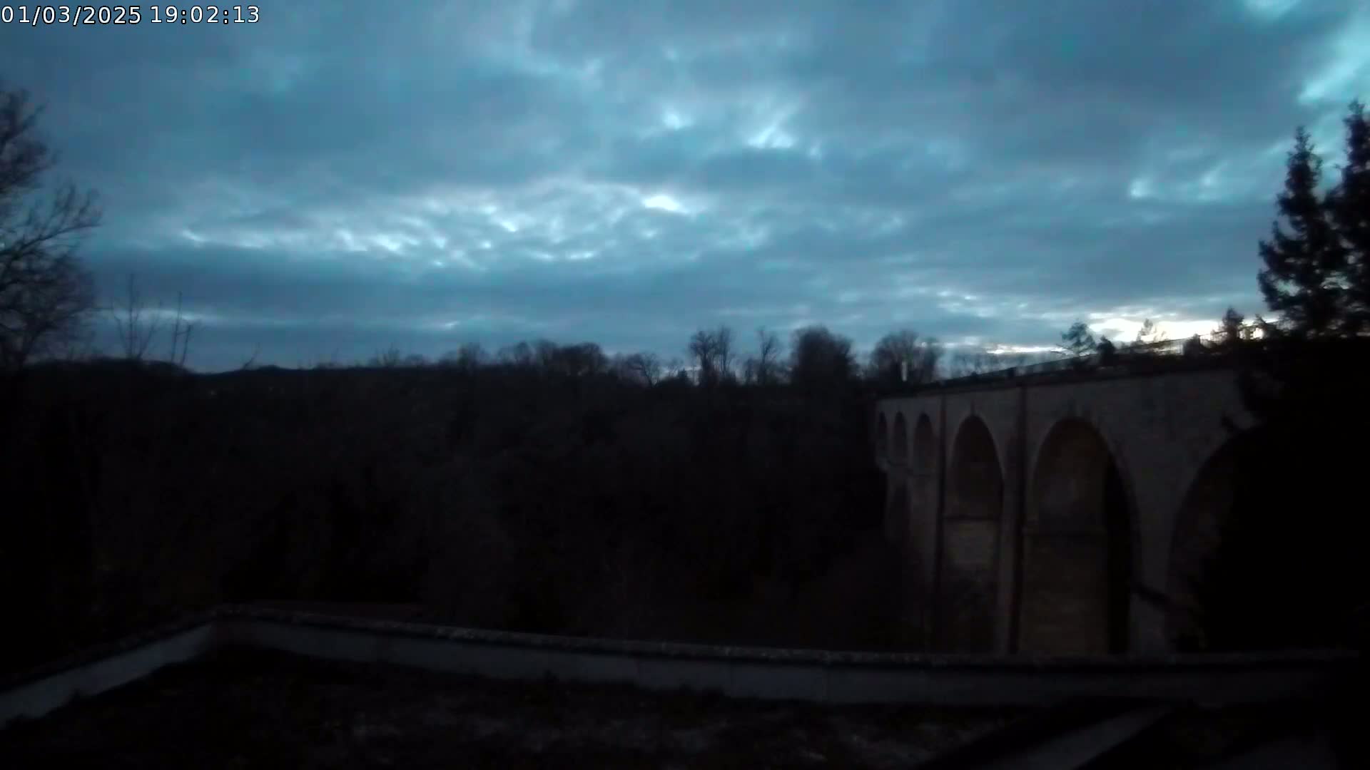 A large stone viaduct is partially visible at dusk under a mostly cloudy sky.