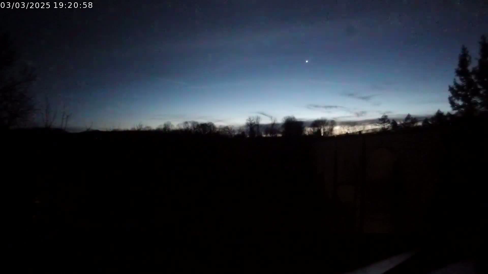 A dark, silhouetted landscape of trees is visible against a twilight sky, with a single bright star or planet in the upper right.