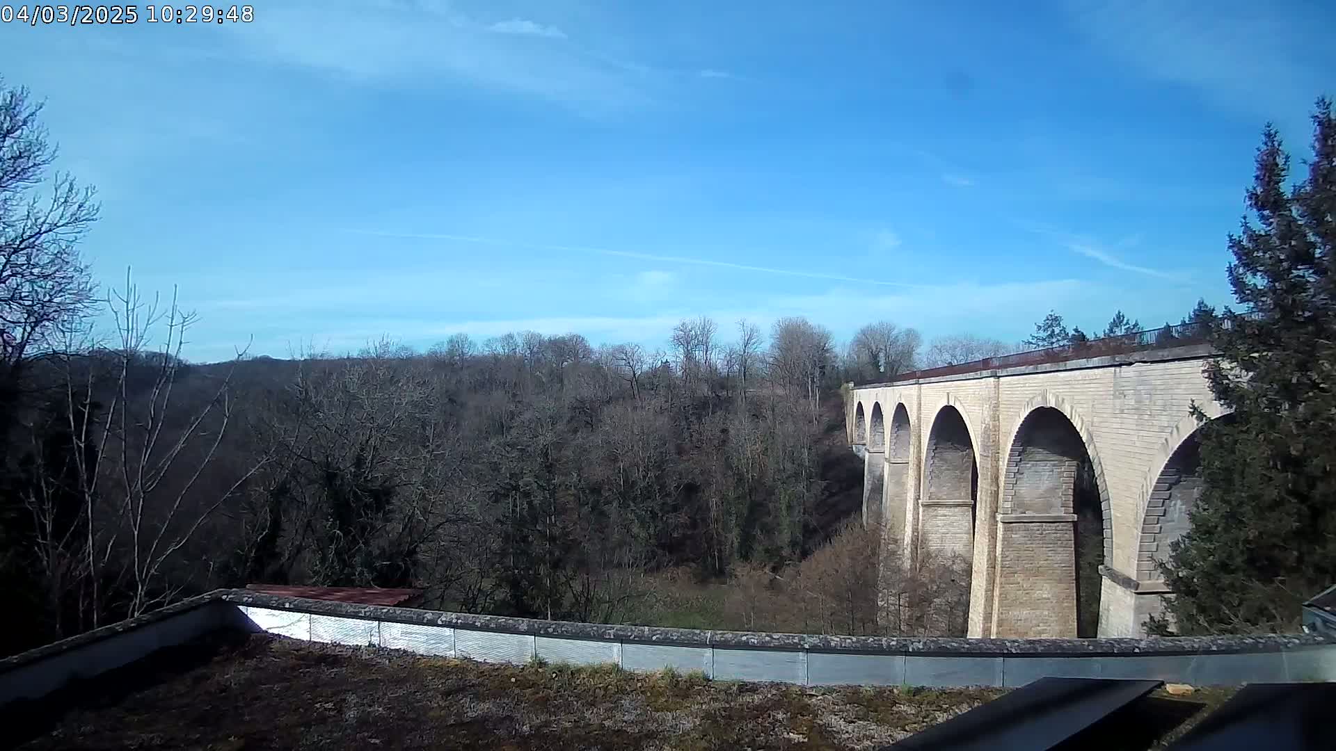 A long stone viaduct stretches across a valley of leafless trees under a mostly clear blue sky.