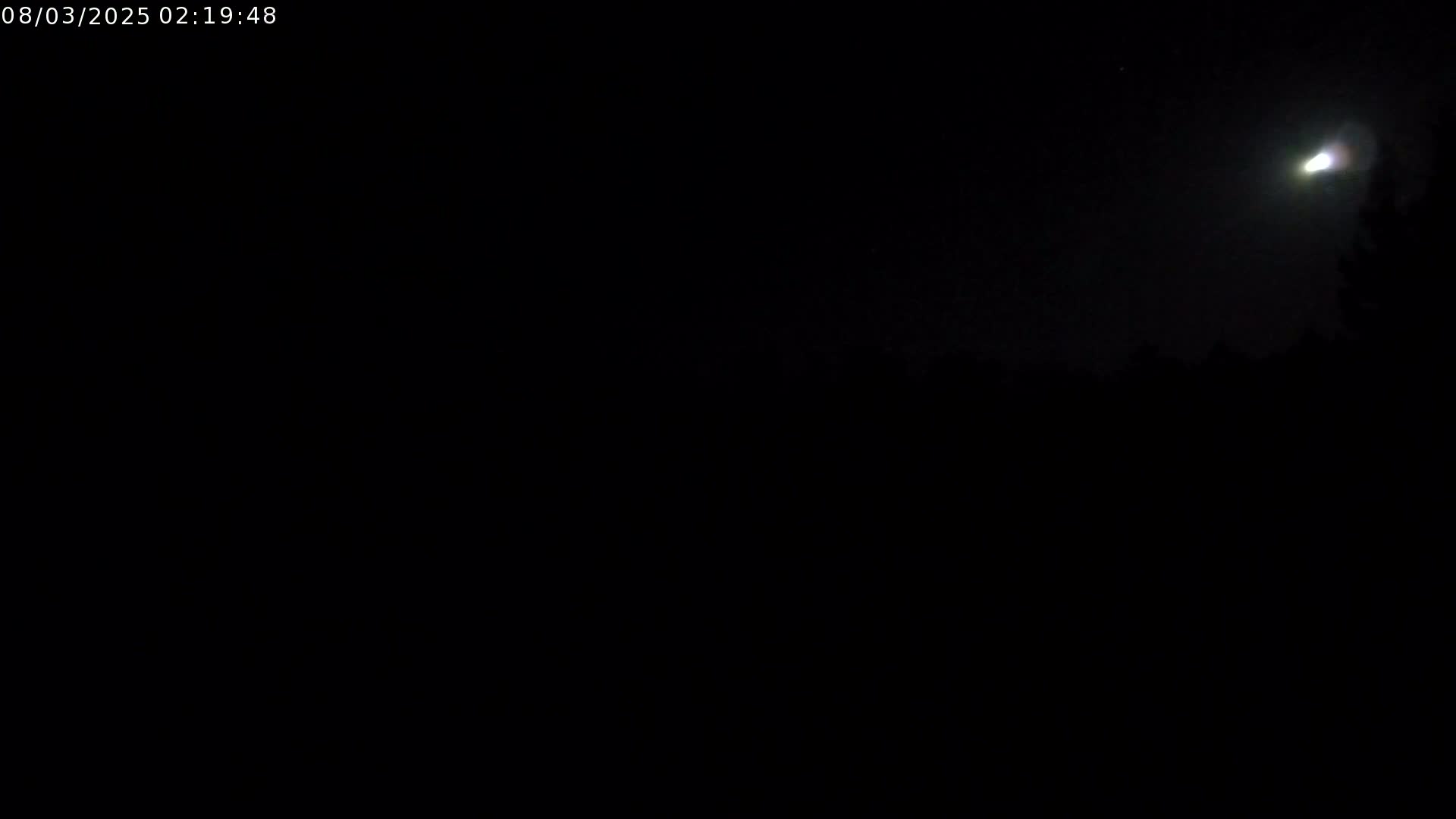 A bright light streaks across a dark night sky above a silhouetted landscape.