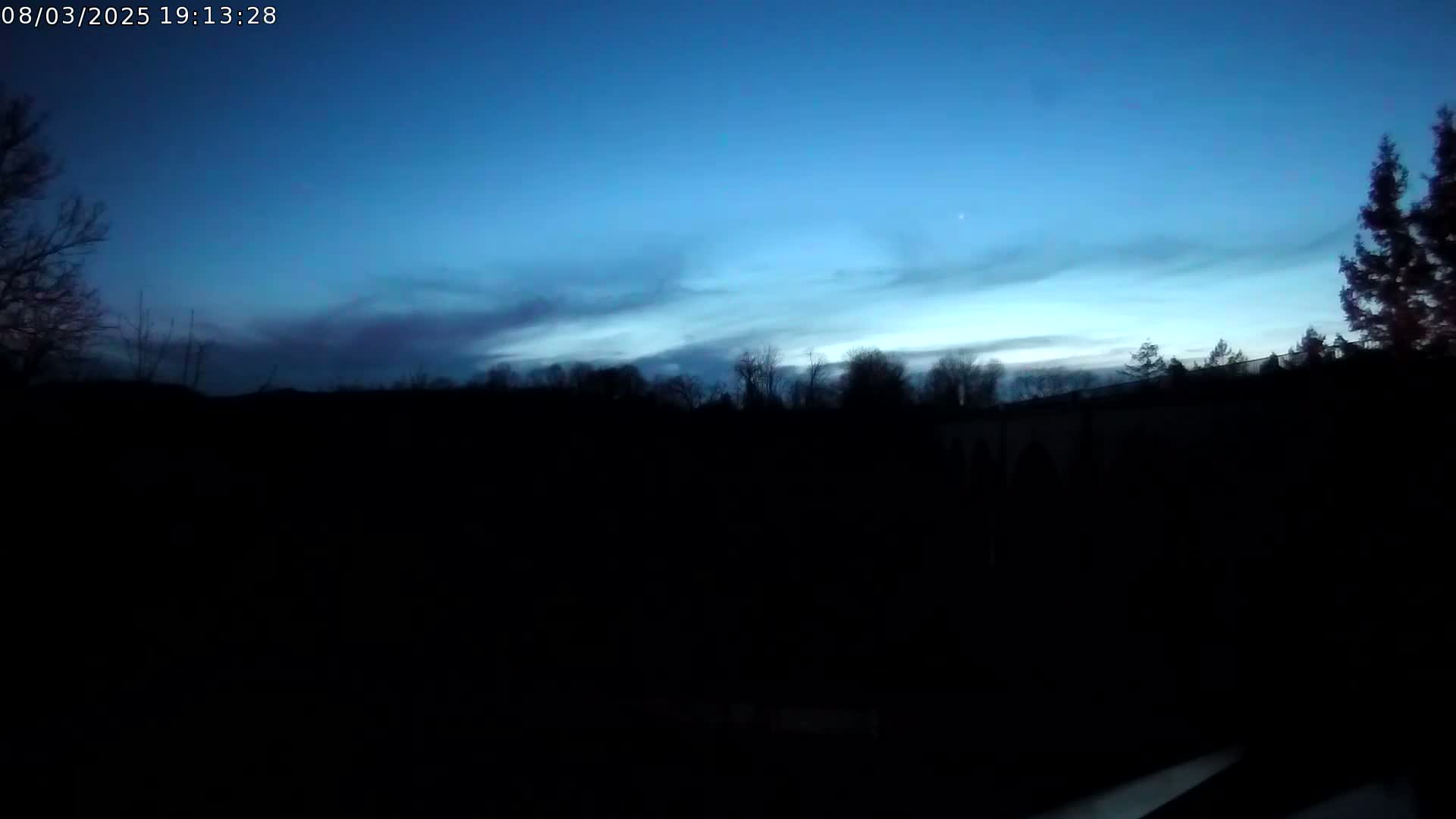 A dark silhouette of trees and a structure is visible against a twilight sky with thin clouds.