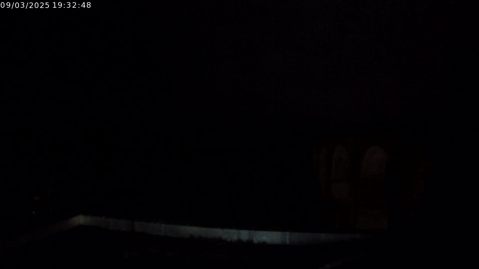 A low-light, nighttime image shows a dark, indistinct background with a faintly visible, light-colored horizontal line near the bottom.