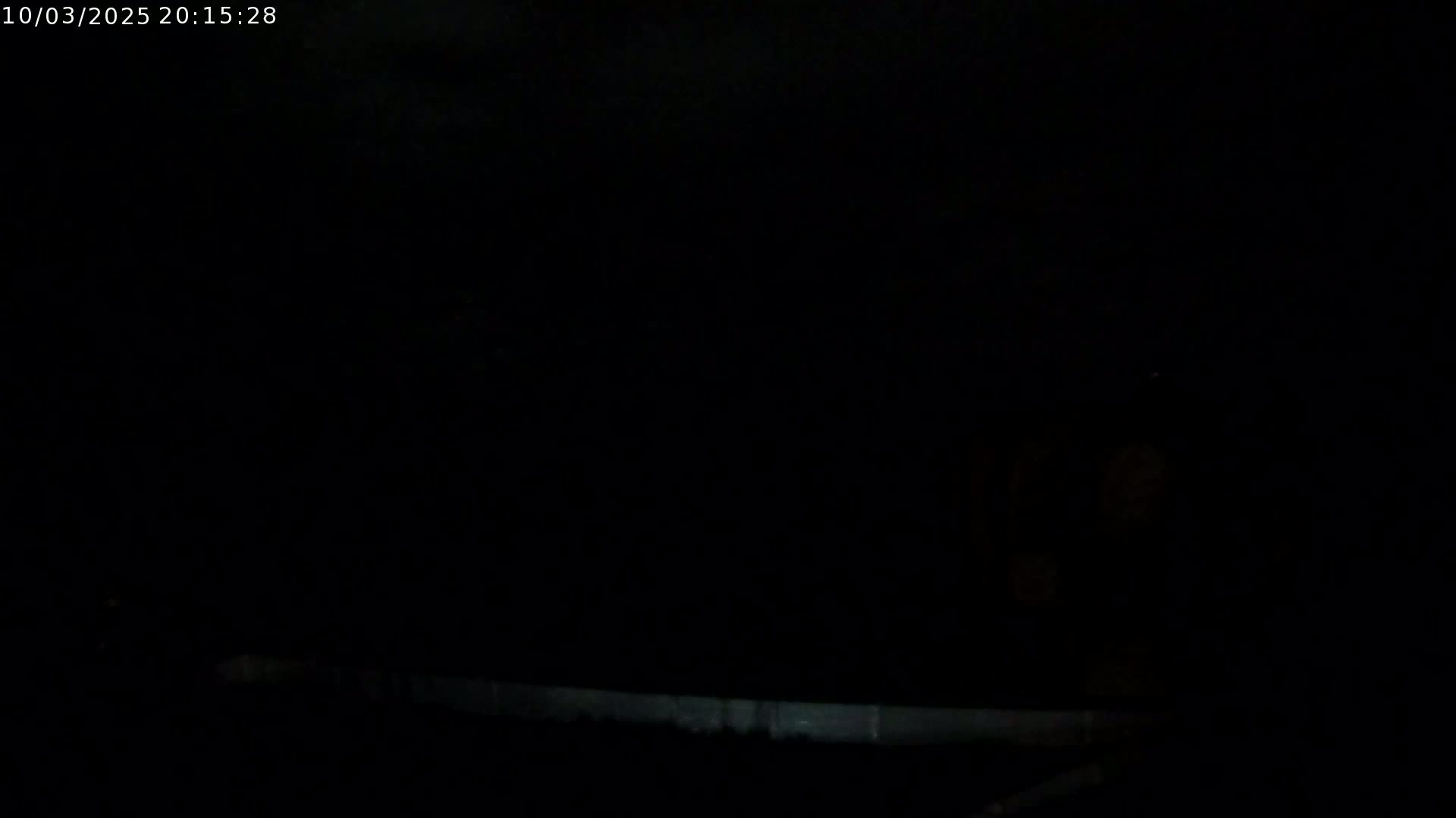 A very dark, nighttime image shows a low, light-colored horizontal line at the bottom, possibly a wall or fence, against an almost completely black background.