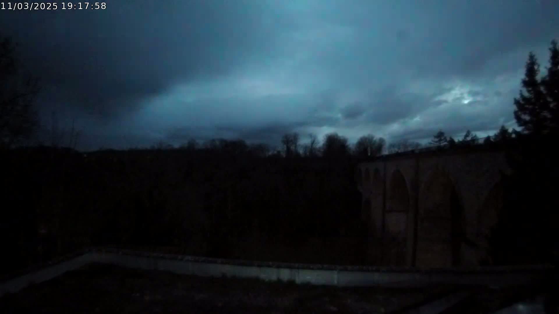 A dark, stone arched bridge is visible in the distance under a twilight sky filled with dark clouds.