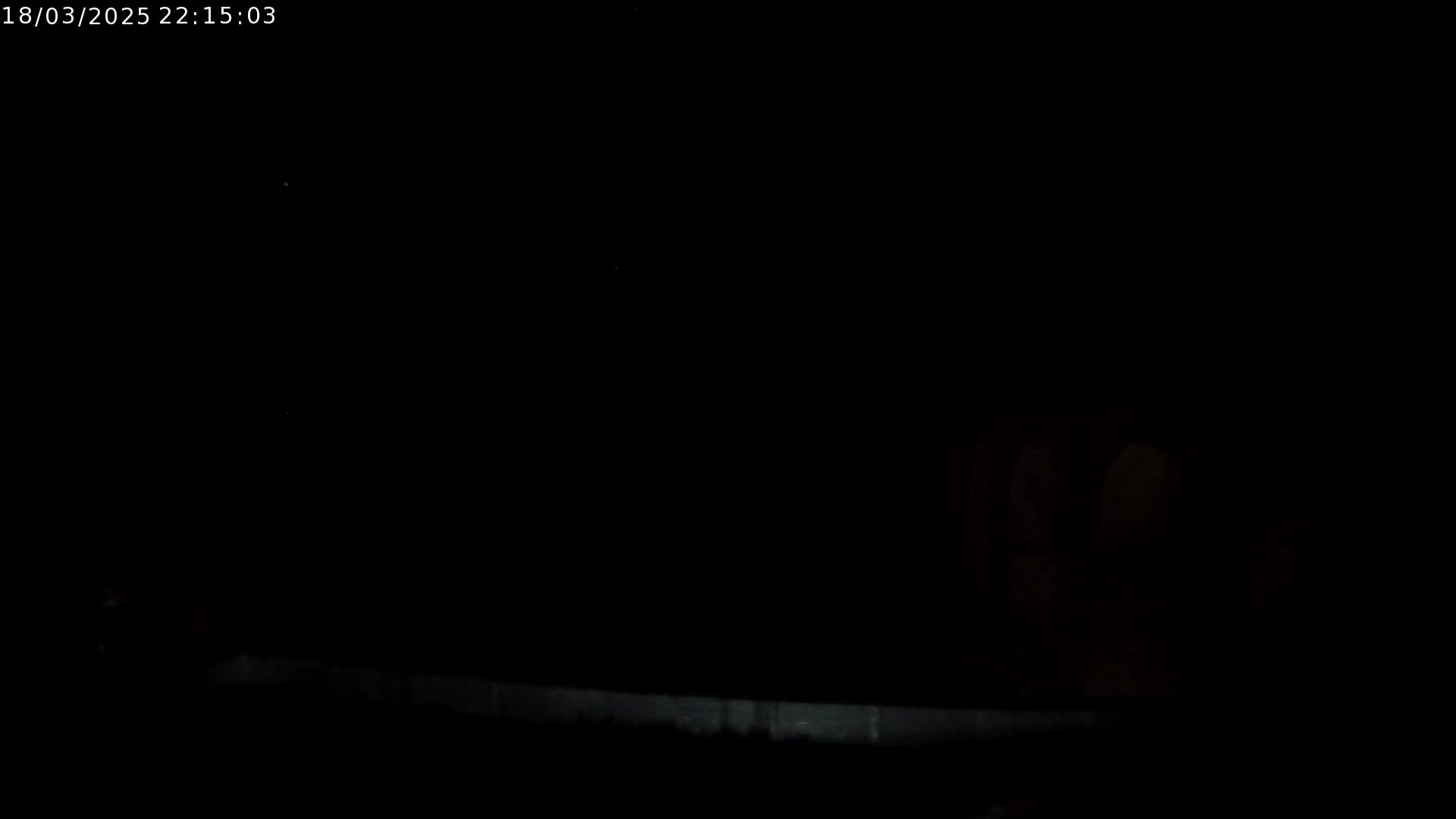 A nighttime, dark scene shows a dimly lit low wall or fence.