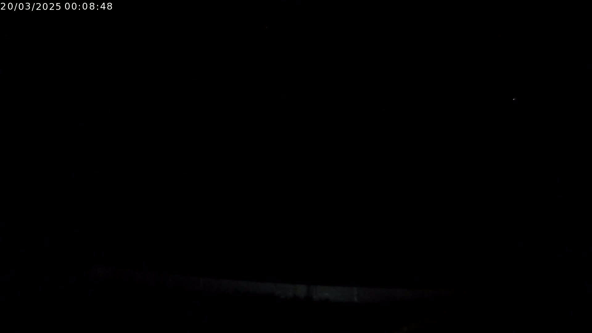 A very dark, nighttime scene shows a dimly lit horizontal line near the bottom, possibly a fence or wall, against a completely black sky.