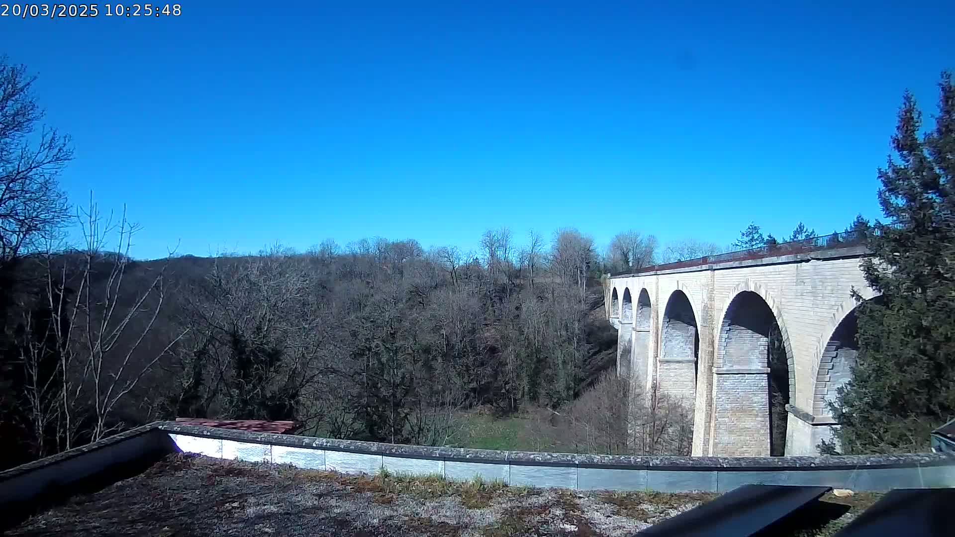 A stone viaduct stretches across a valley of leafless trees under a clear blue sky.