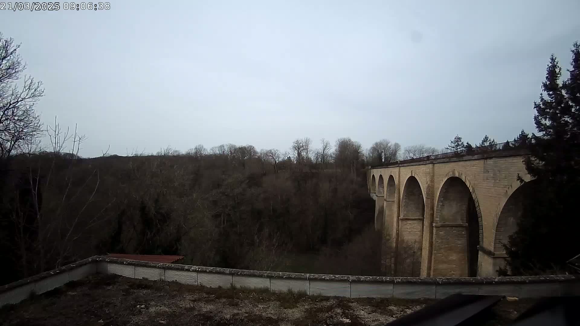 A stone viaduct with multiple arches spans a wooded valley under an overcast sky.
