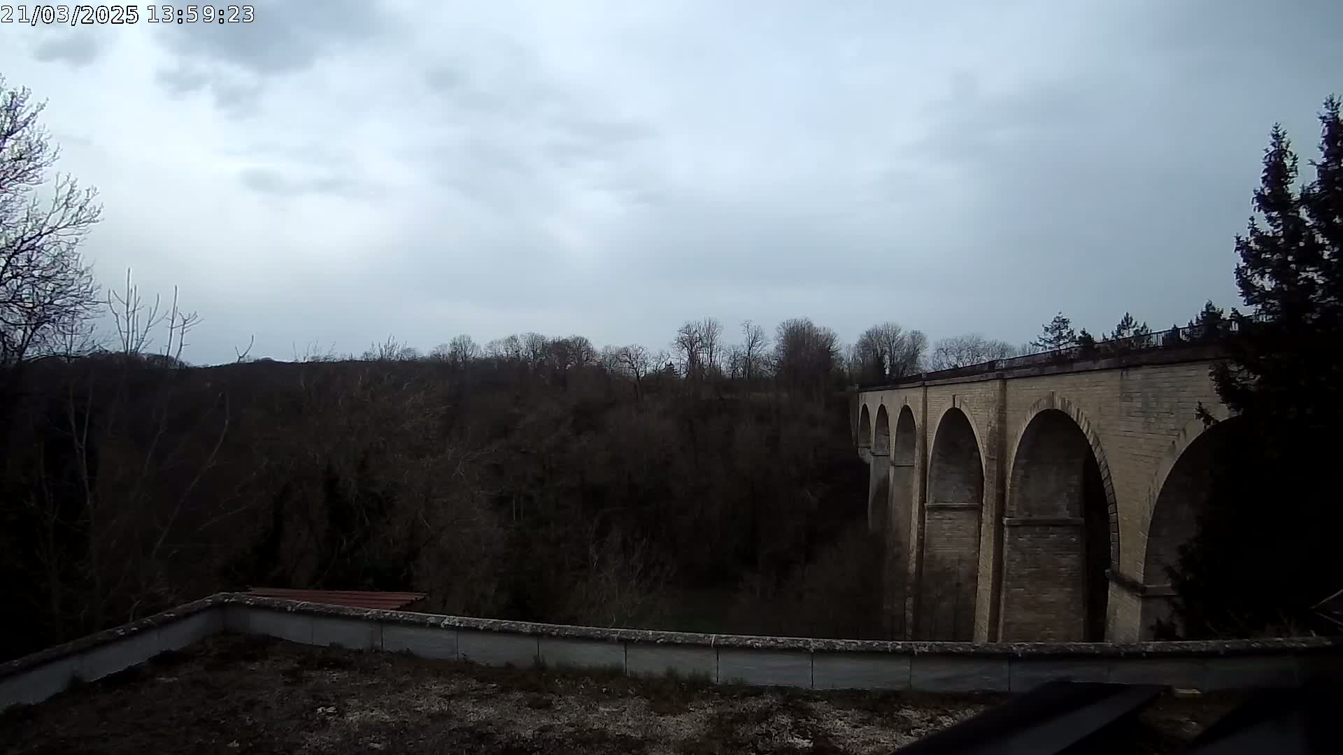 A stone viaduct stretches across a wooded valley under a cloudy sky.