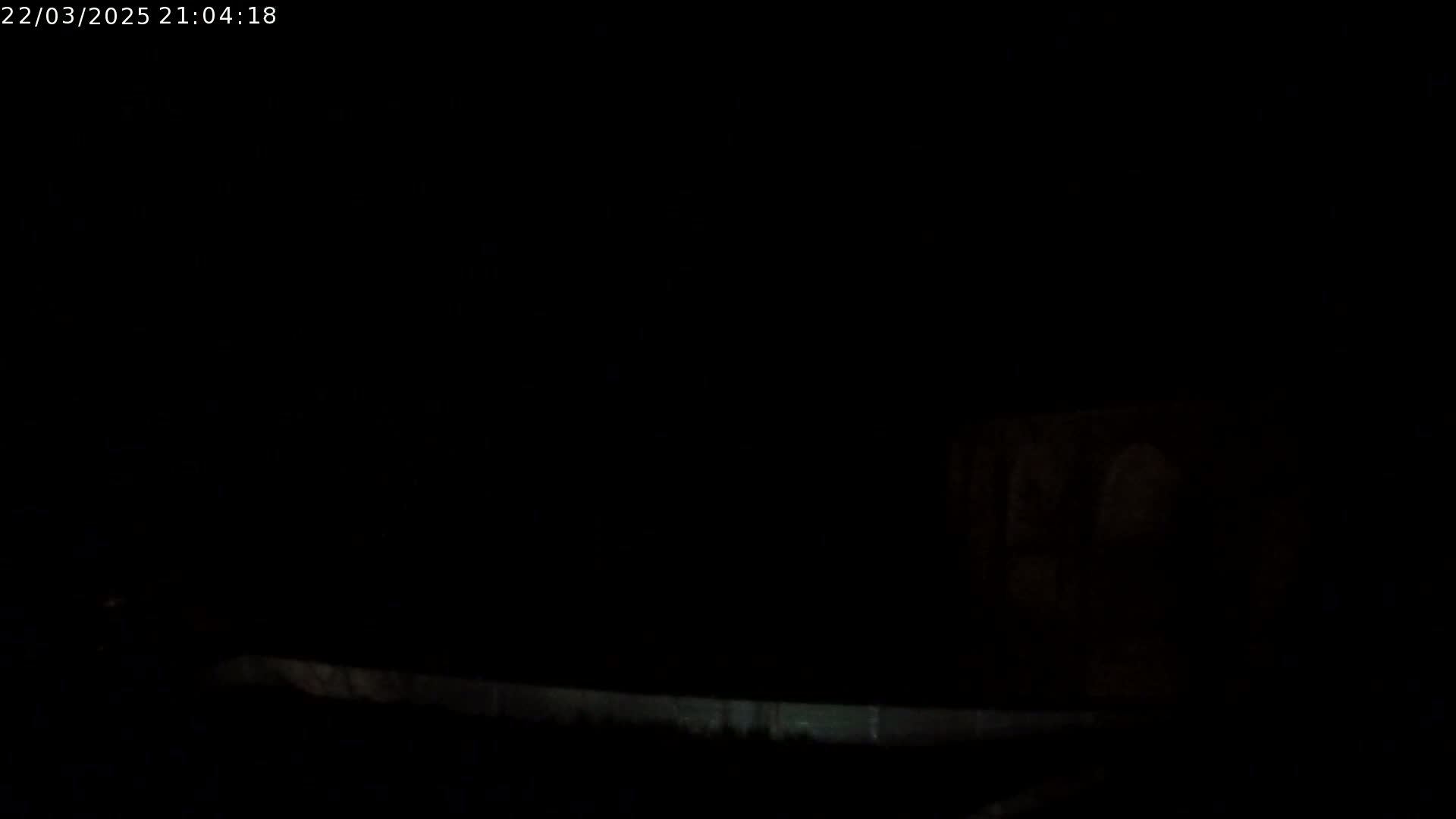 A dark, nighttime scene shows a dimly lit structure in the distance.
