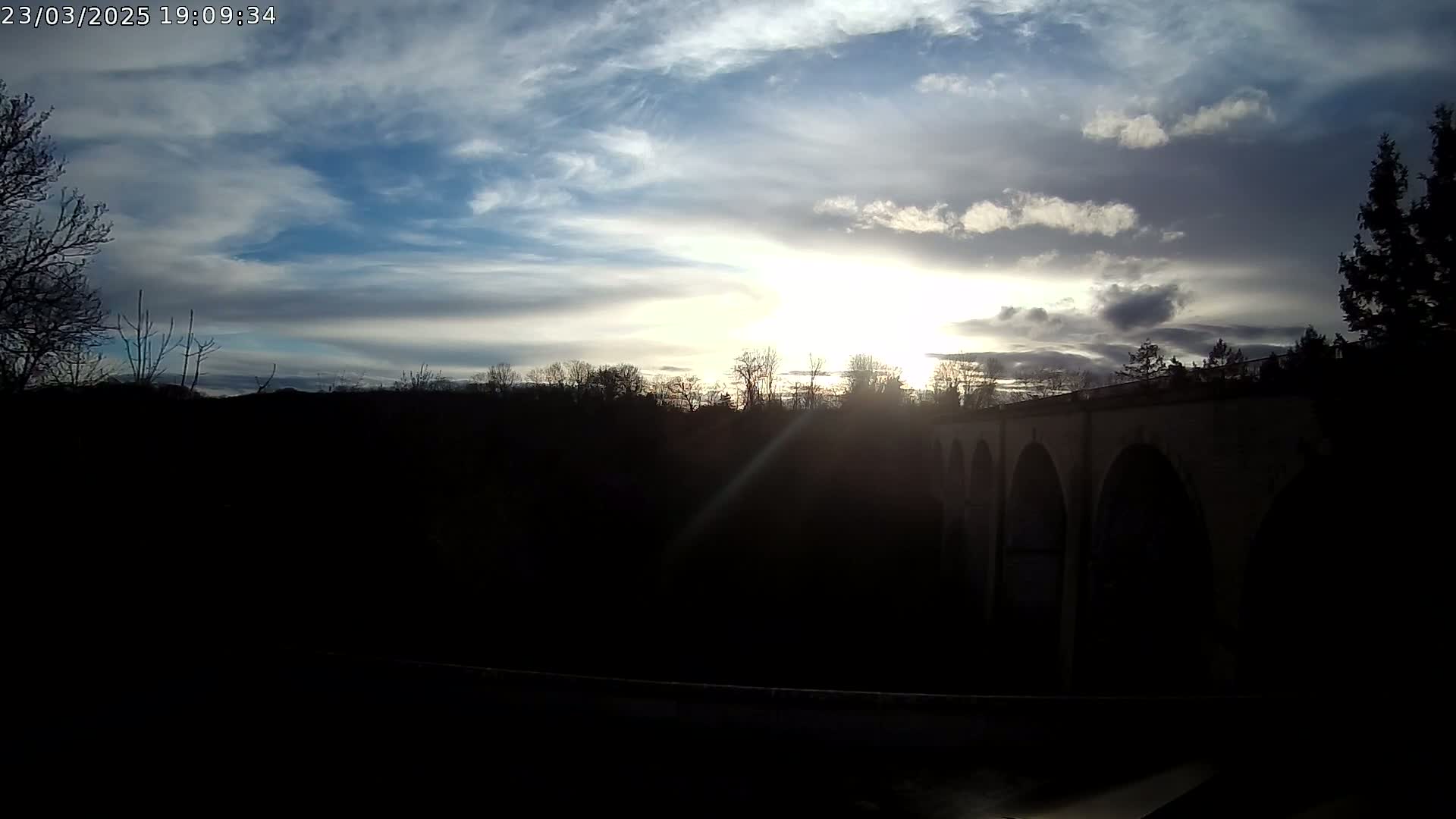 A stone viaduct is silhouetted against a partly cloudy sunset.