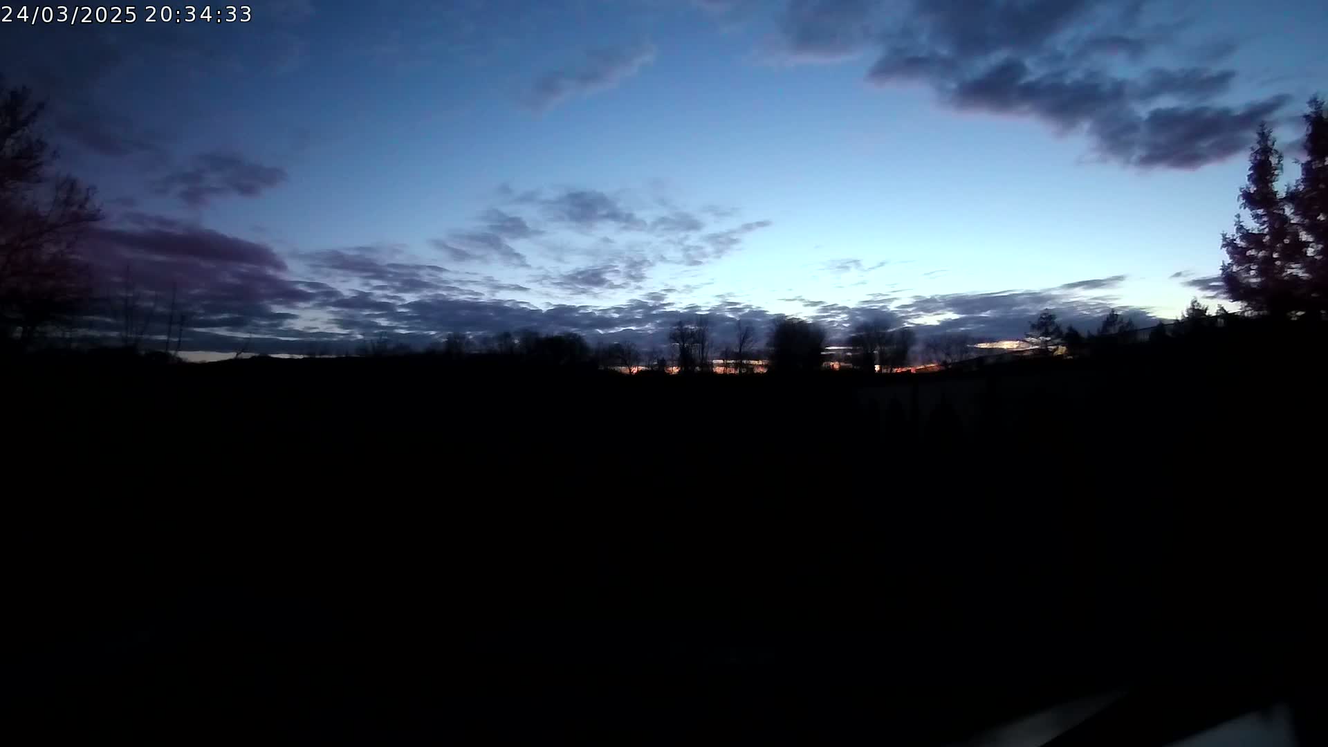 A dark, silhouetted landscape of trees is visible against a twilight sky filled with clouds showing hints of orange and pink near the horizon.