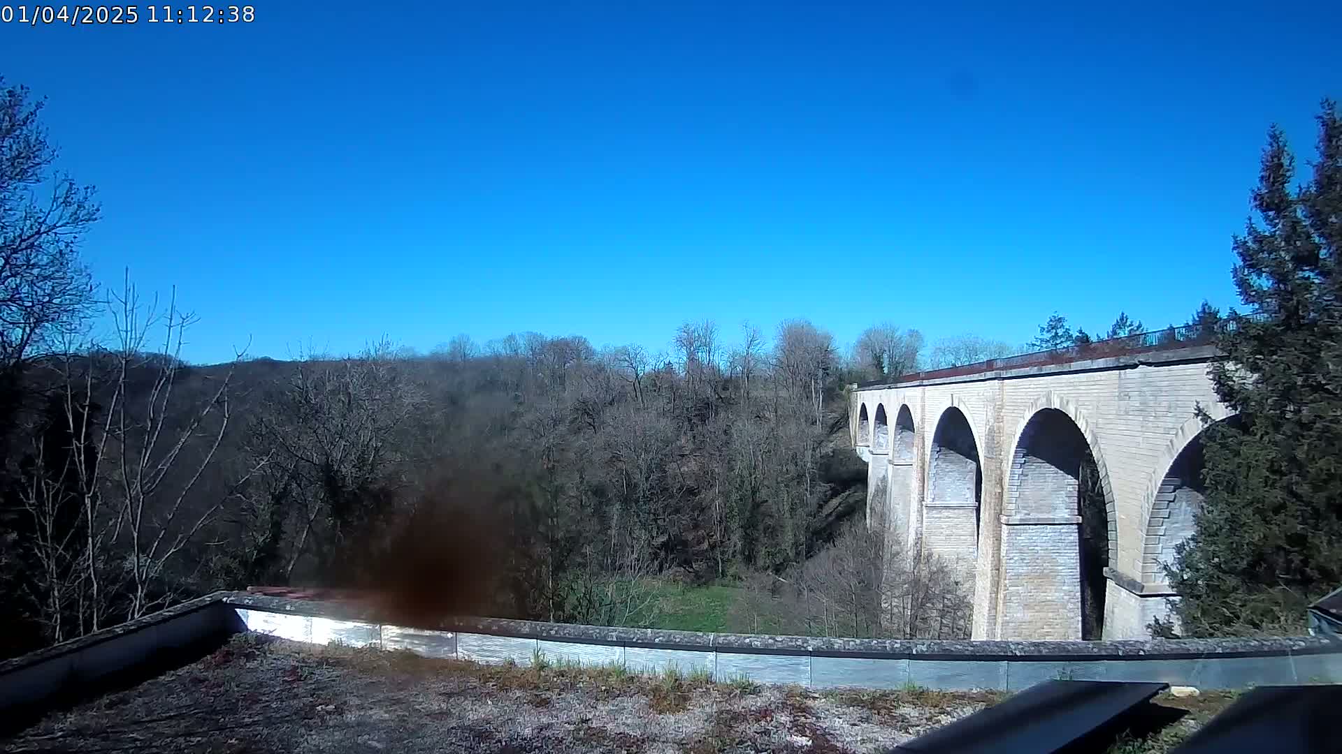 A stone viaduct stretches across a valley of bare trees under a clear blue sky.