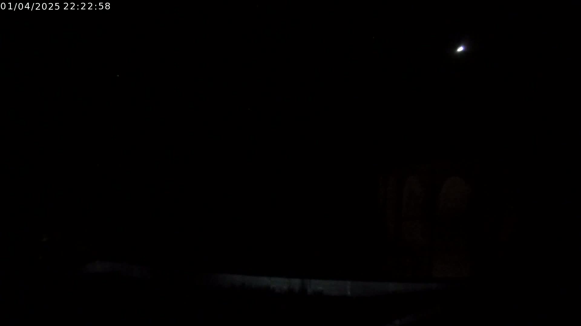A nighttime, outdoor scene shows a faintly illuminated moon and dark, indistinct shapes in the distance under a clear sky.