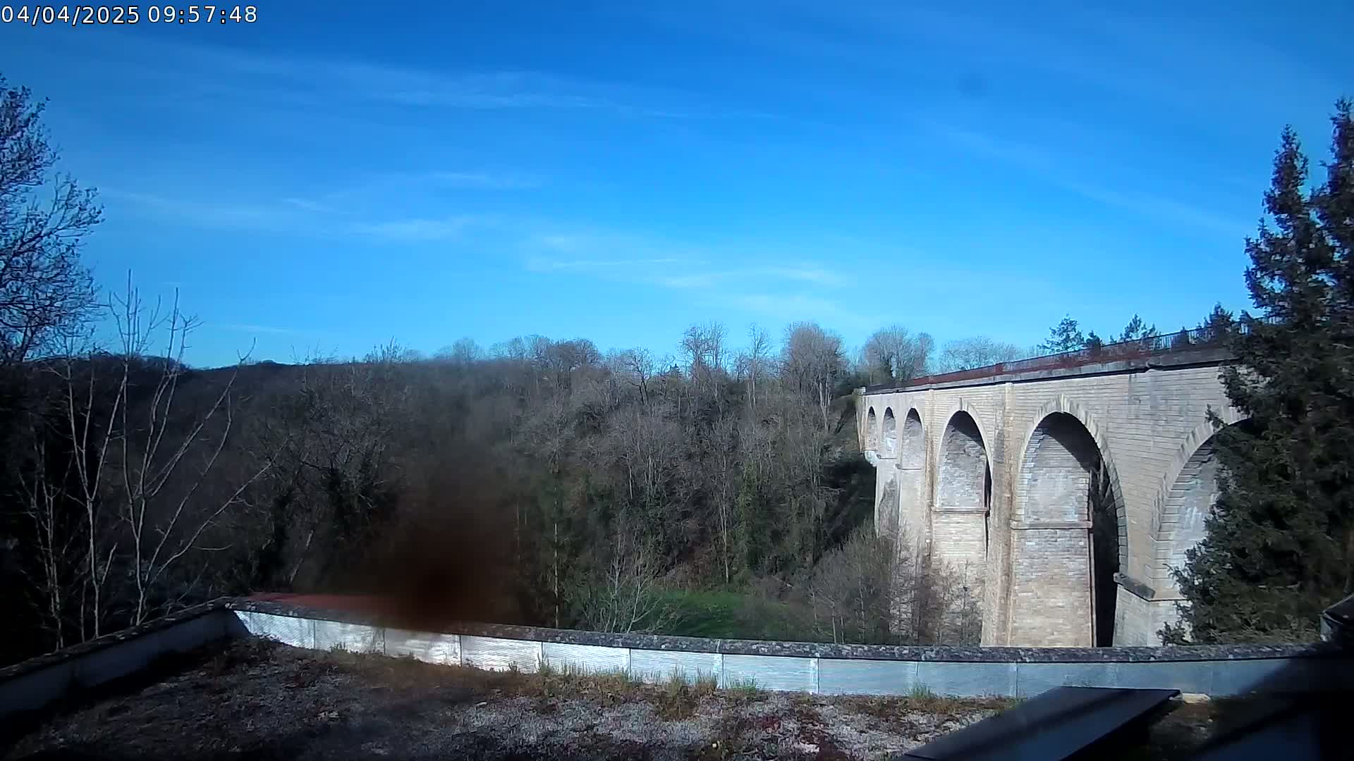 A stone viaduct stretches across a valley of leafless trees under a clear blue sky.