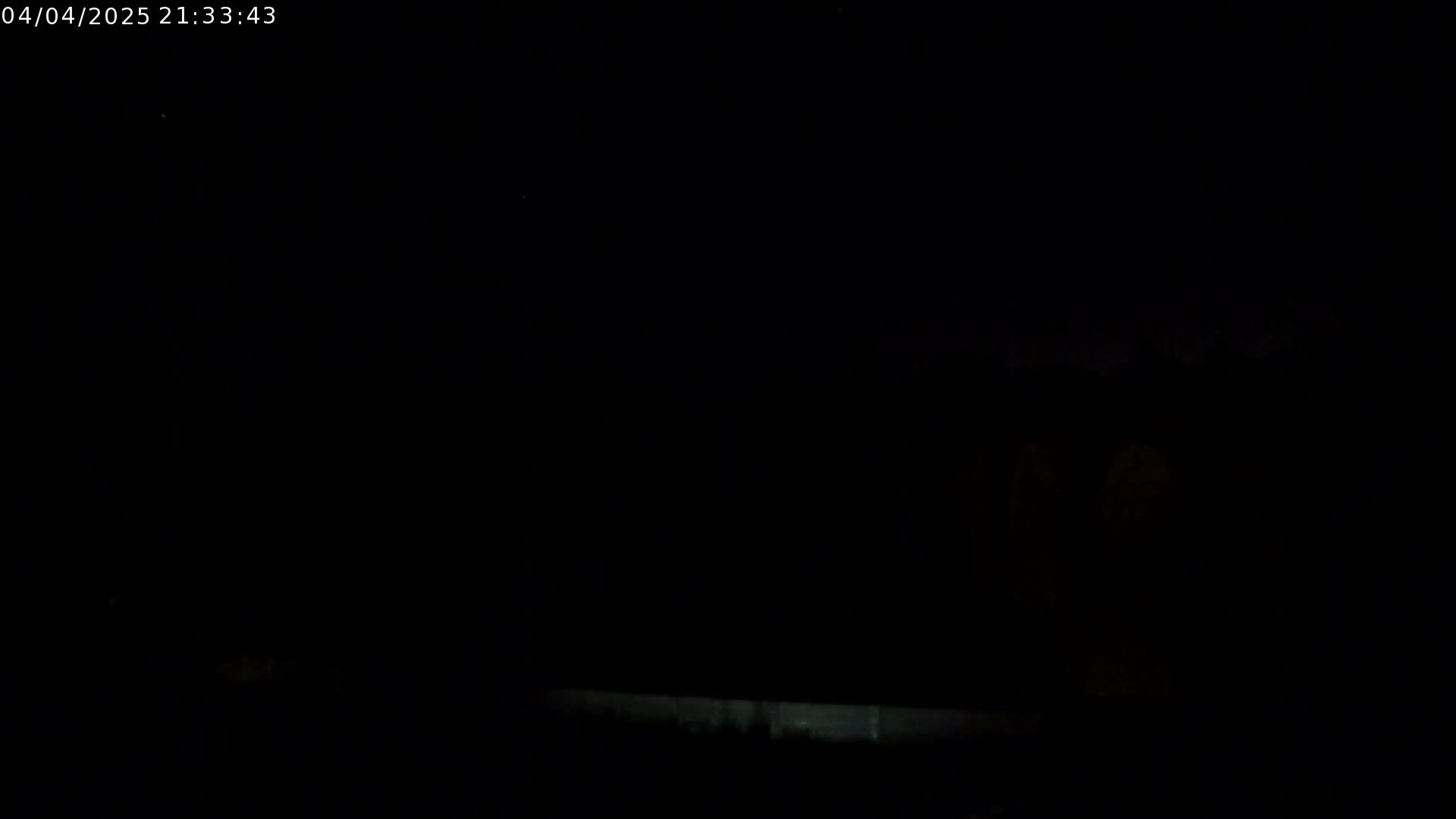 A dark, nighttime scene shows a low horizon line with indistinct shapes in the distance under a completely black sky.