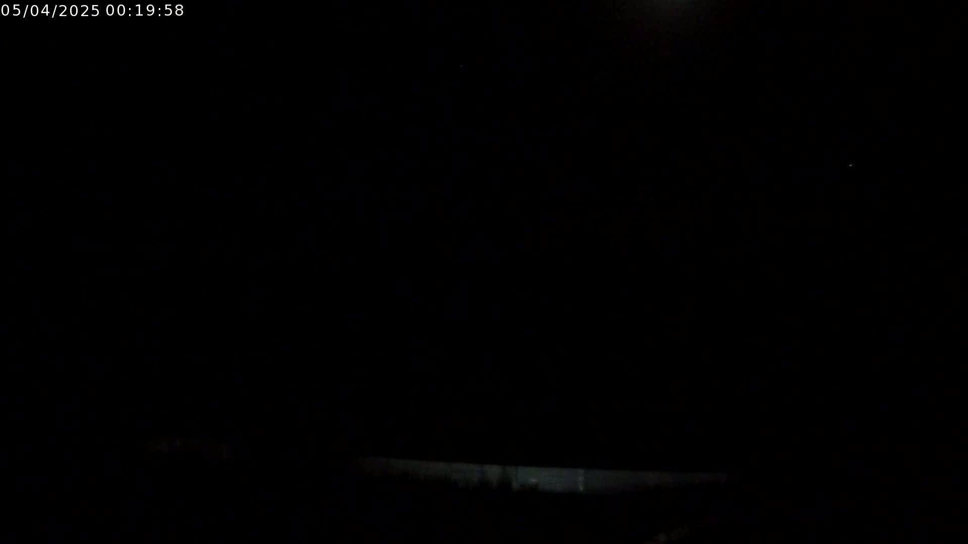 A low-light outdoor image shows a dark, mostly clear night sky with a faint, bright area possibly the moon.