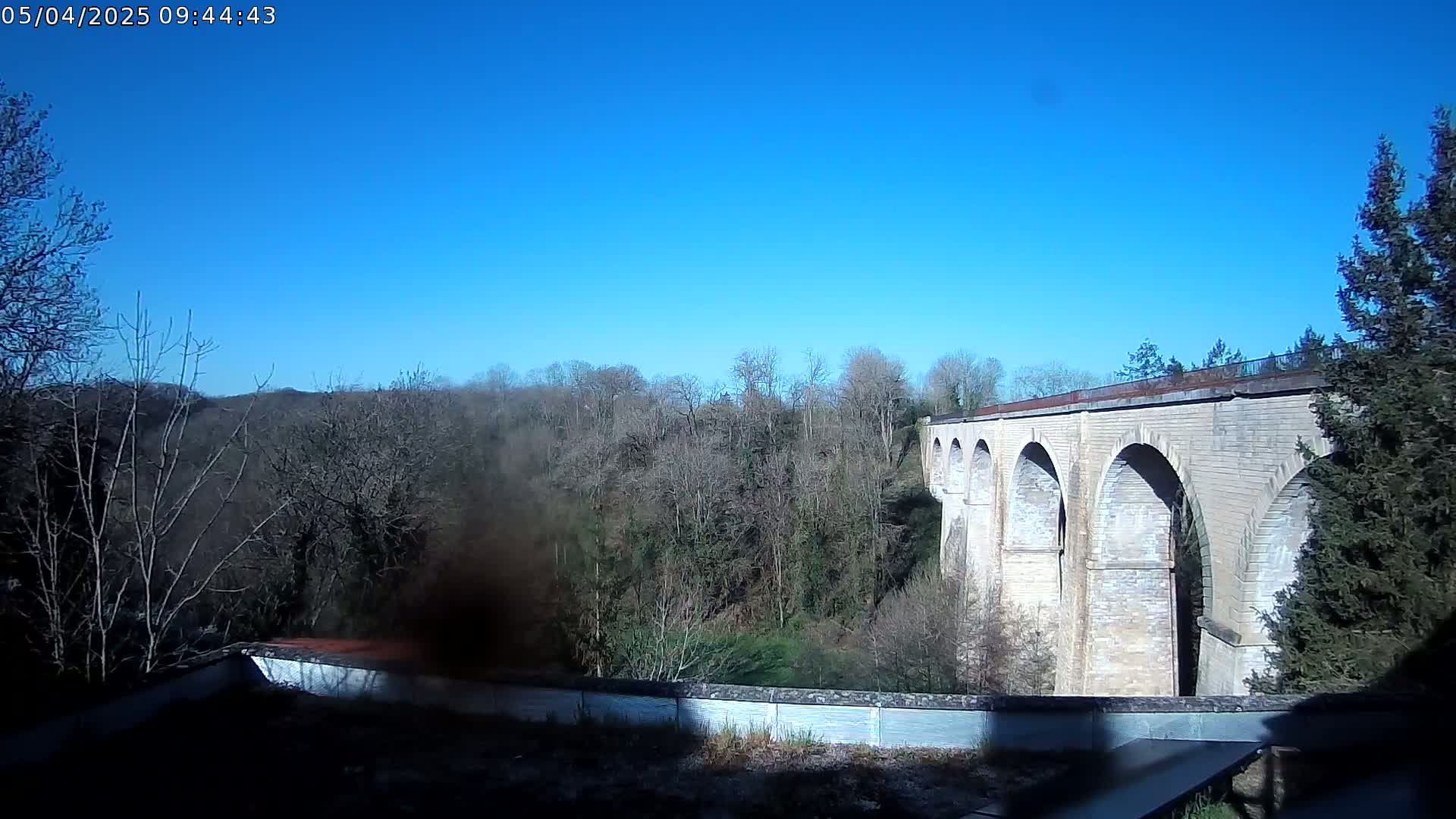 A stone viaduct stretches across a valley of leafless trees under a clear blue sky.