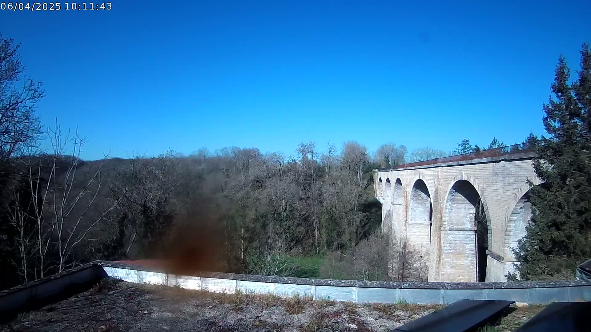 A stone viaduct stretches across a valley of leafless trees under a clear blue sky.