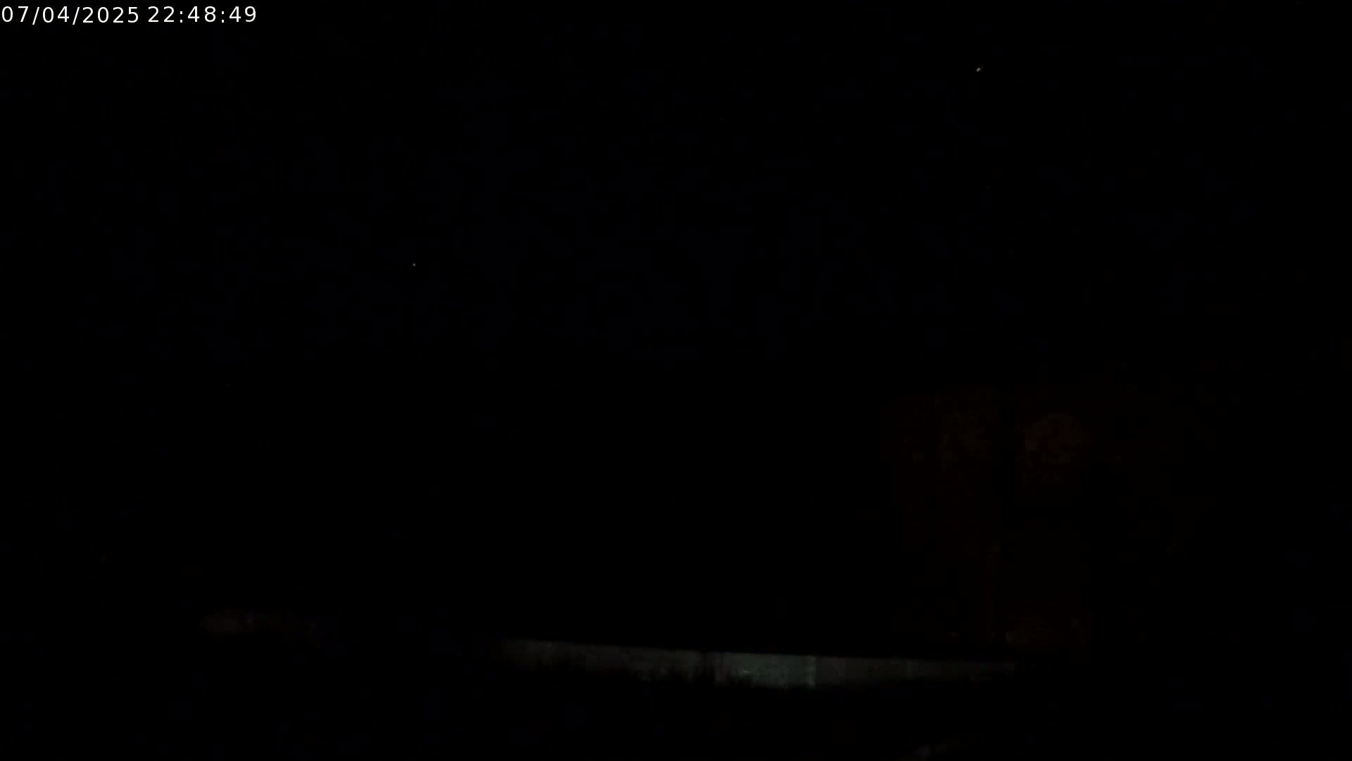 A low-light nighttime outdoor scene shows a dark sky with a few faint lights, possibly stars, and a dark ground with a low, light-colored horizontal line near the bottom.