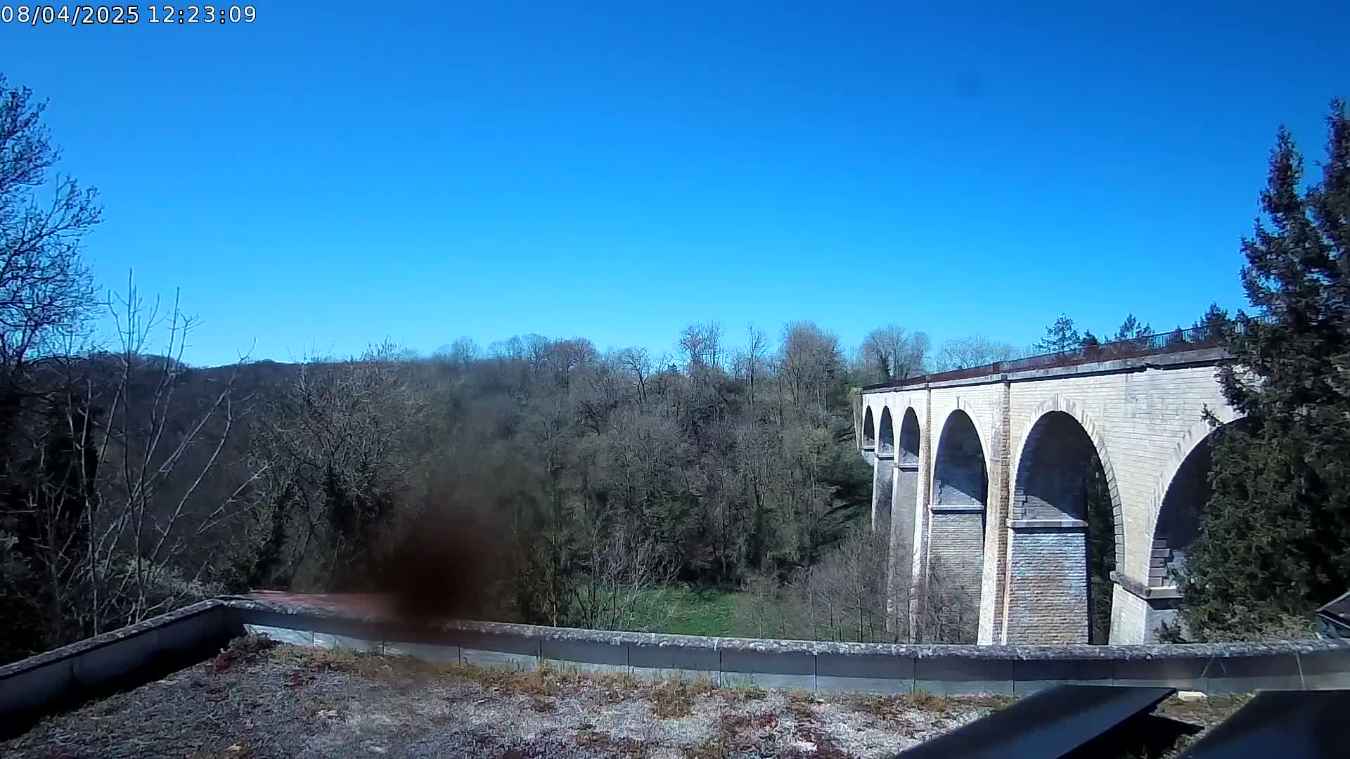 A stone viaduct with multiple arches spans a valley of bare trees under a clear blue sky.
