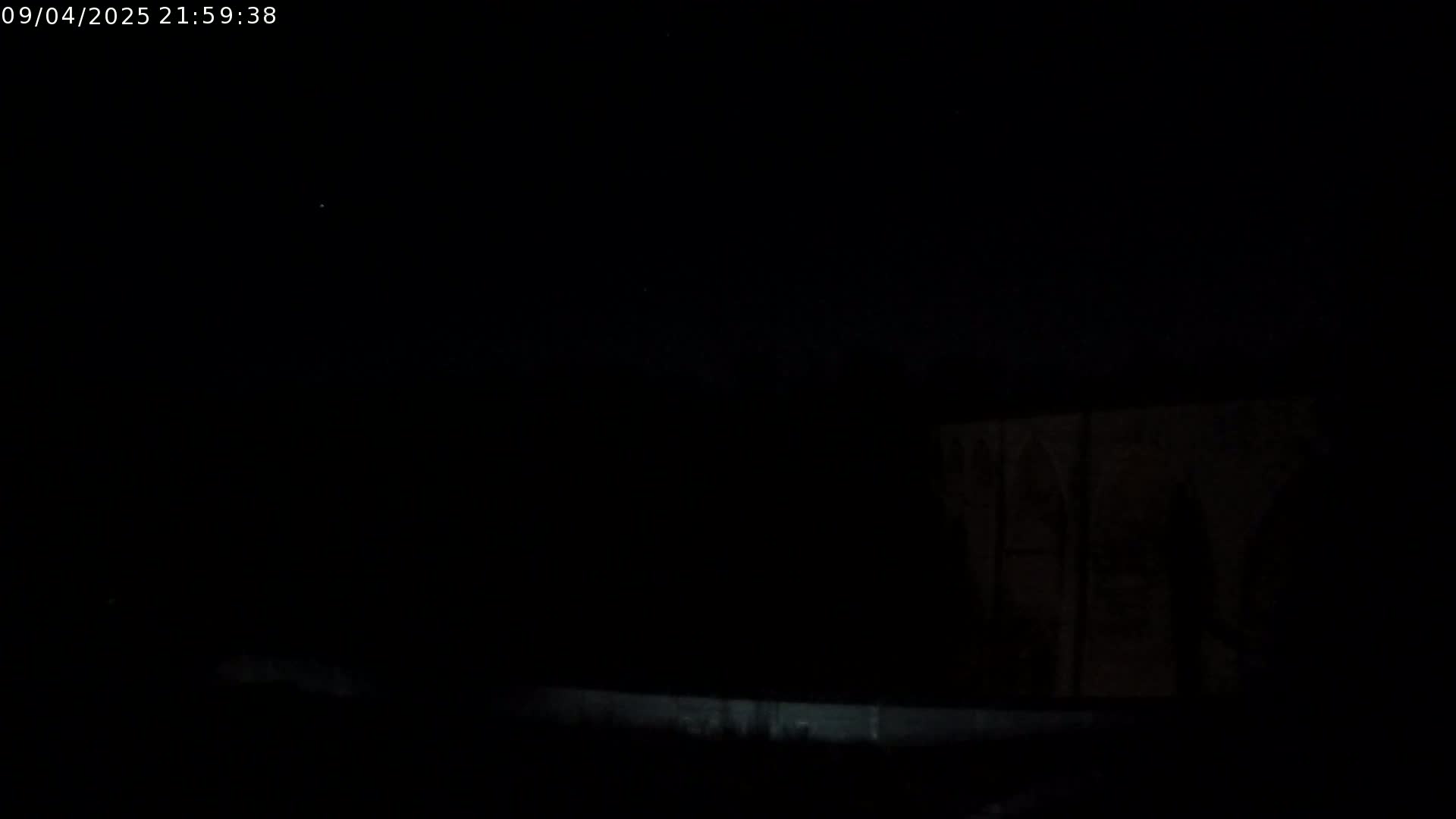 A dark, nighttime scene shows a dimly lit structure in the distance under a mostly clear sky.