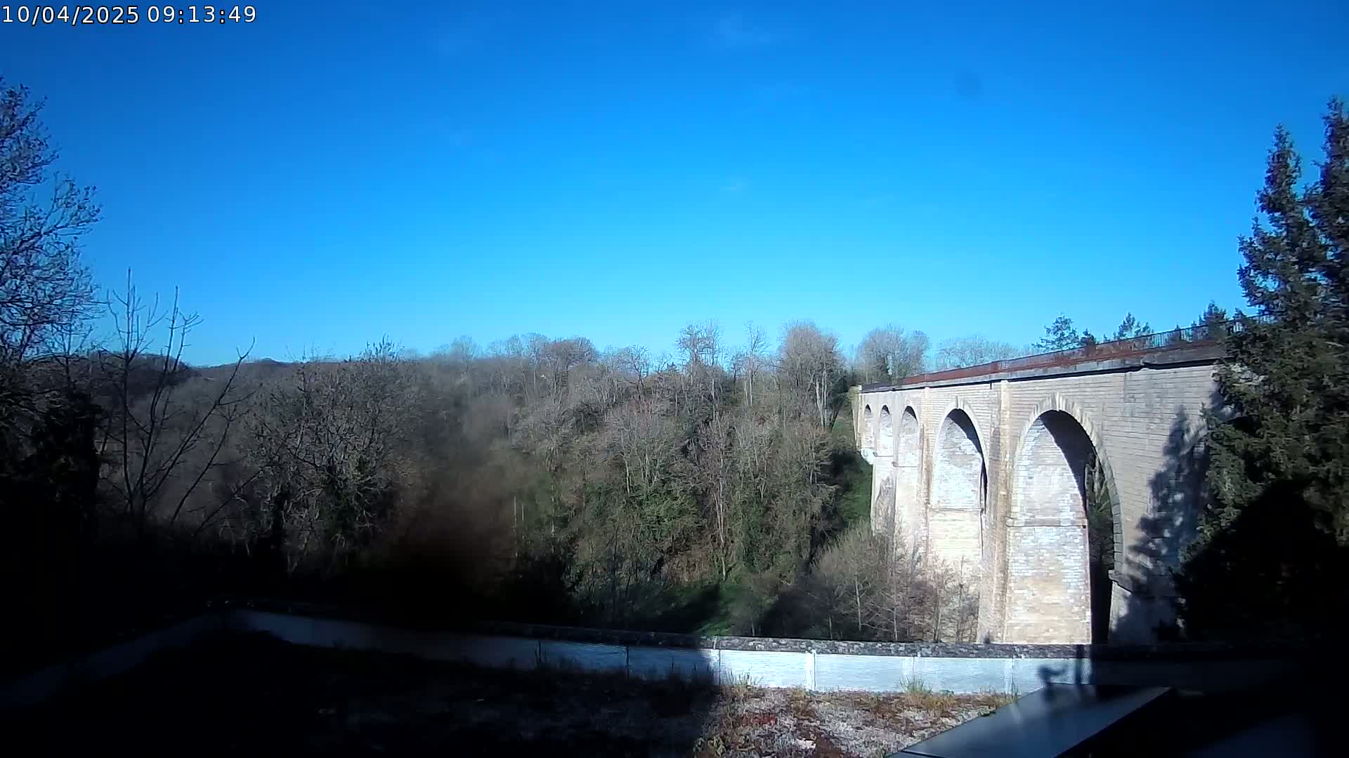 A stone viaduct with multiple arches stretches across a wooded valley under a clear blue sky.