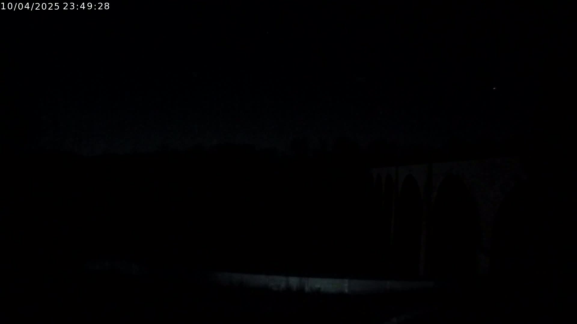 A dark, nighttime scene shows a portion of a structure with arches silhouetted against a mostly clear sky.