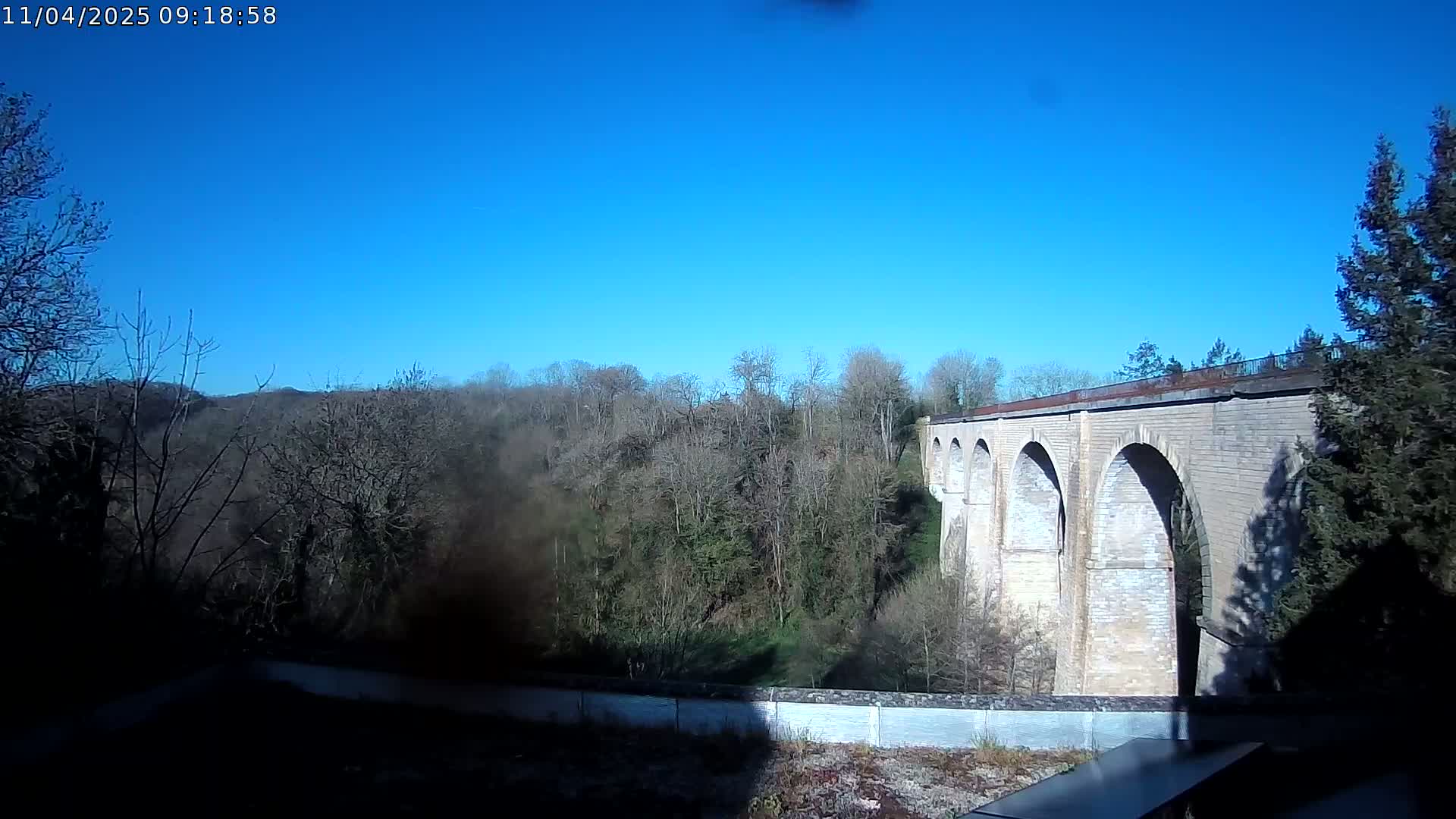 A stone viaduct stretches across a valley of leafless trees under a clear blue sky.