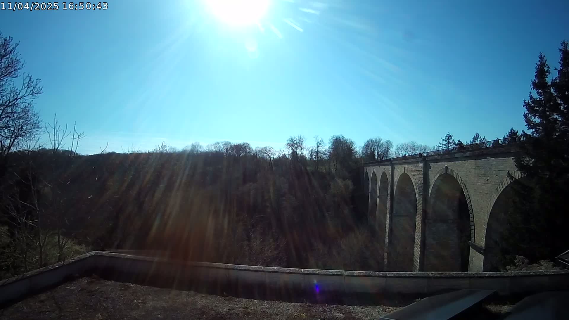 A stone viaduct stretches across a wooded valley under a bright, sunny sky.