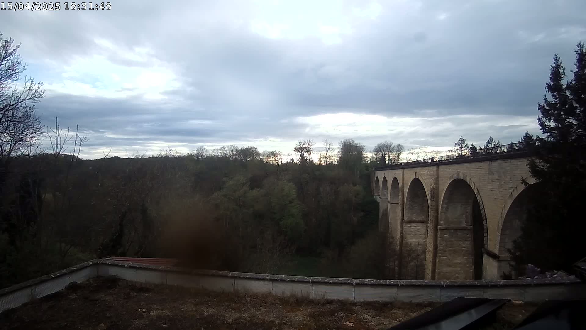 A stone viaduct stretches across a valley of leafless trees under a partly cloudy sky.