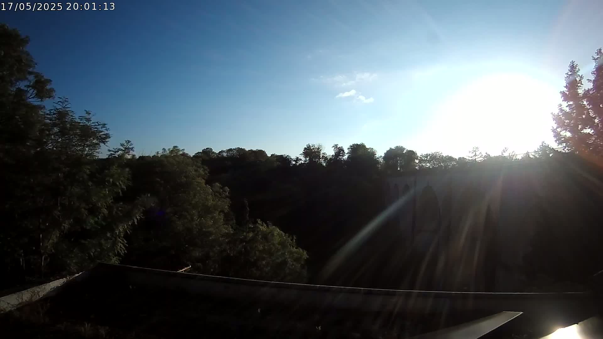 A stone bridge is partially visible through trees under a bright, mostly sunny sky.