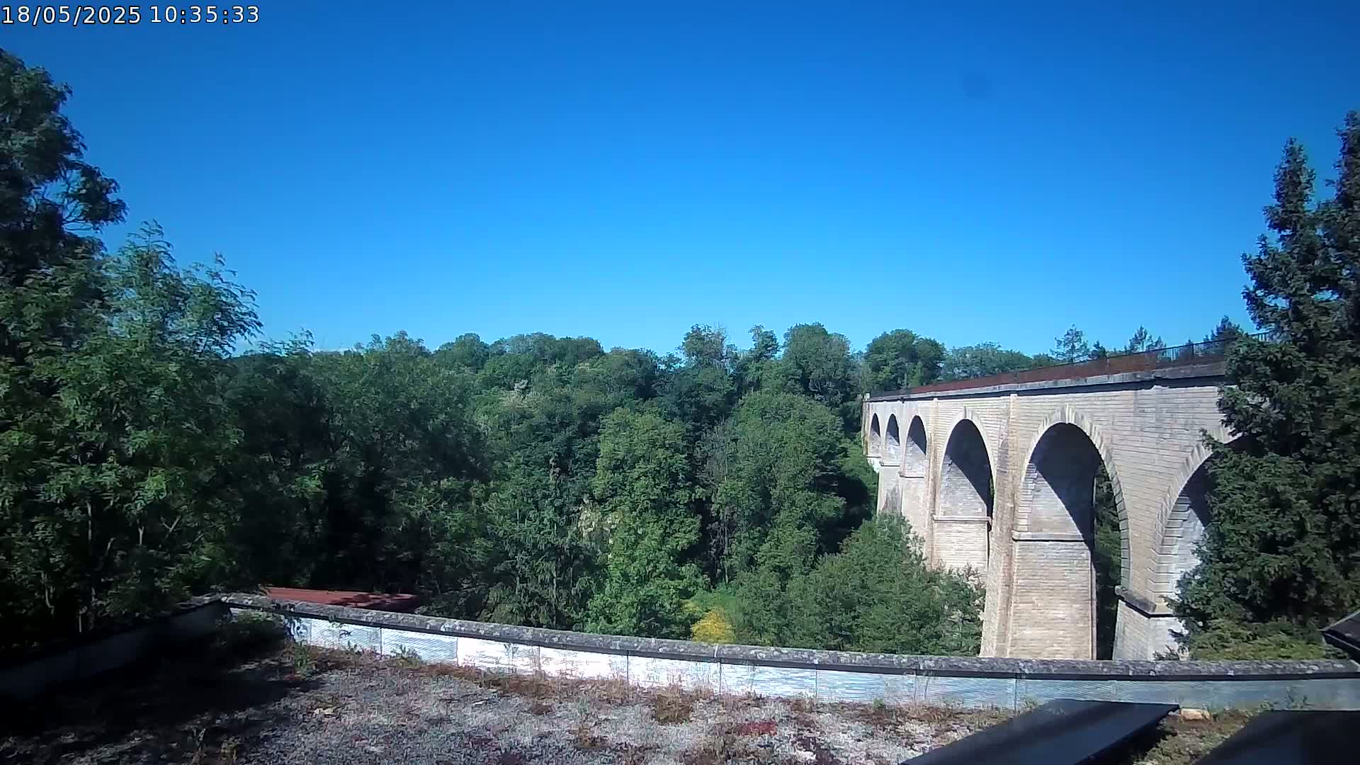A stone viaduct with multiple arches stretches across a lush green valley under a clear blue sky.