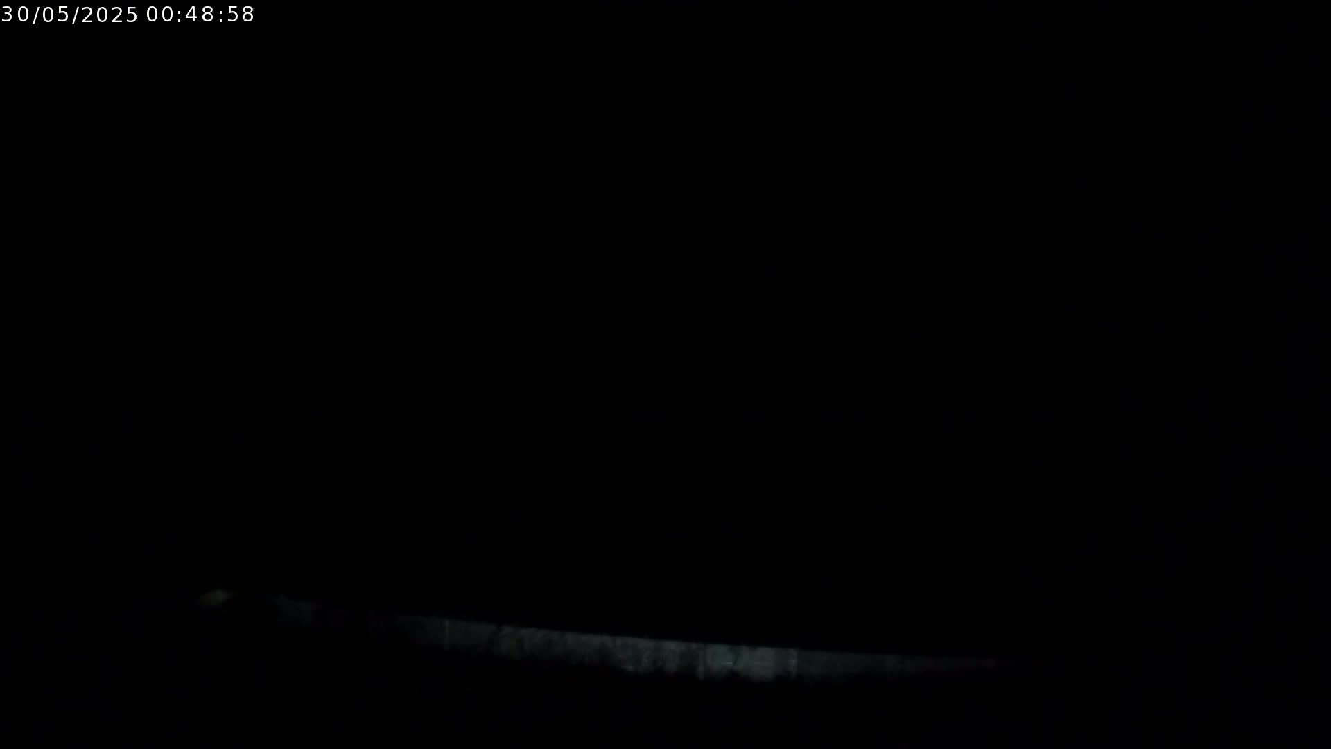 A very low-light image shows a faint, horizontal line near the bottom, suggesting a low-lying object or surface in the dark.