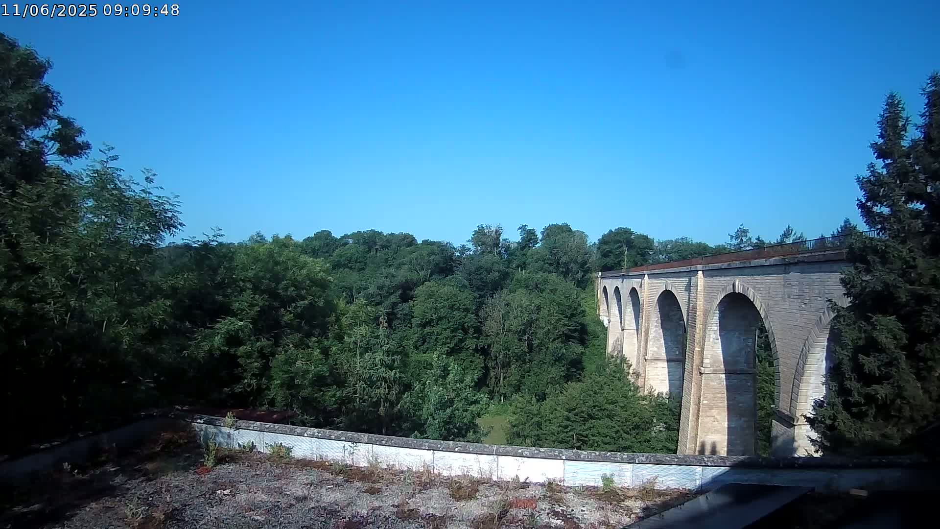 A stone viaduct stretches across a lush green valley under a clear blue sky.