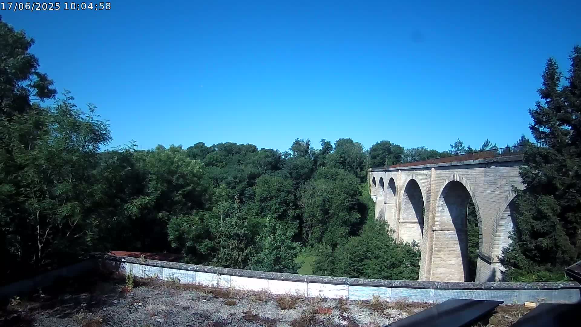 A stone viaduct stretches across a lush green valley under a clear blue sky.