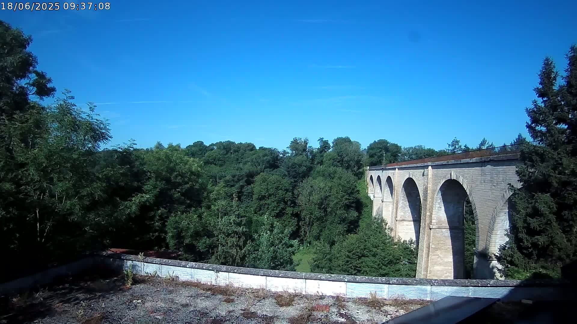 A stone viaduct stretches across a lush green valley under a clear blue sky.