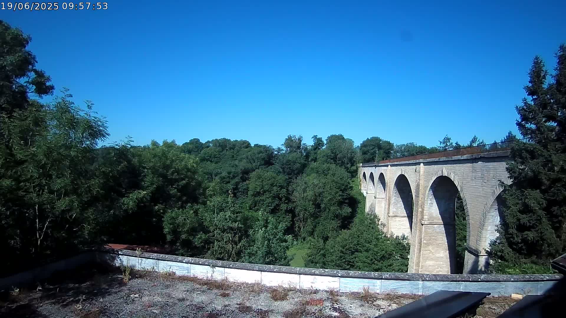 A long stone viaduct stretches across a lush green valley under a clear blue sky.
