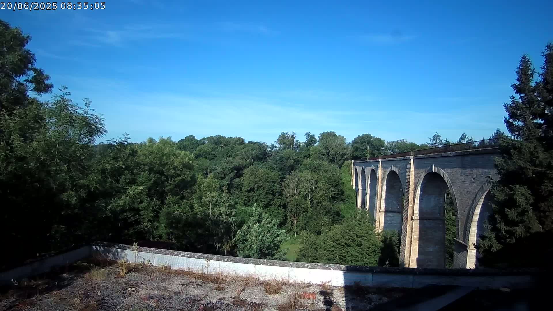 A stone viaduct stretches across a lush green valley under a clear blue sky.