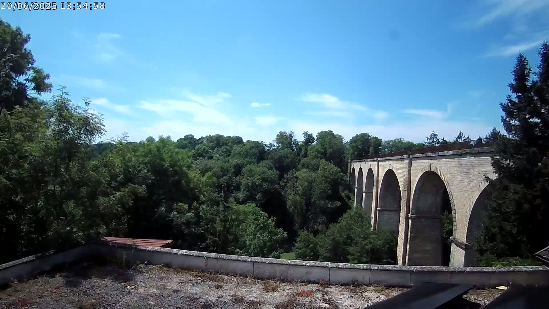 A stone viaduct with multiple arches stretches across a lush green valley under a mostly sunny sky.