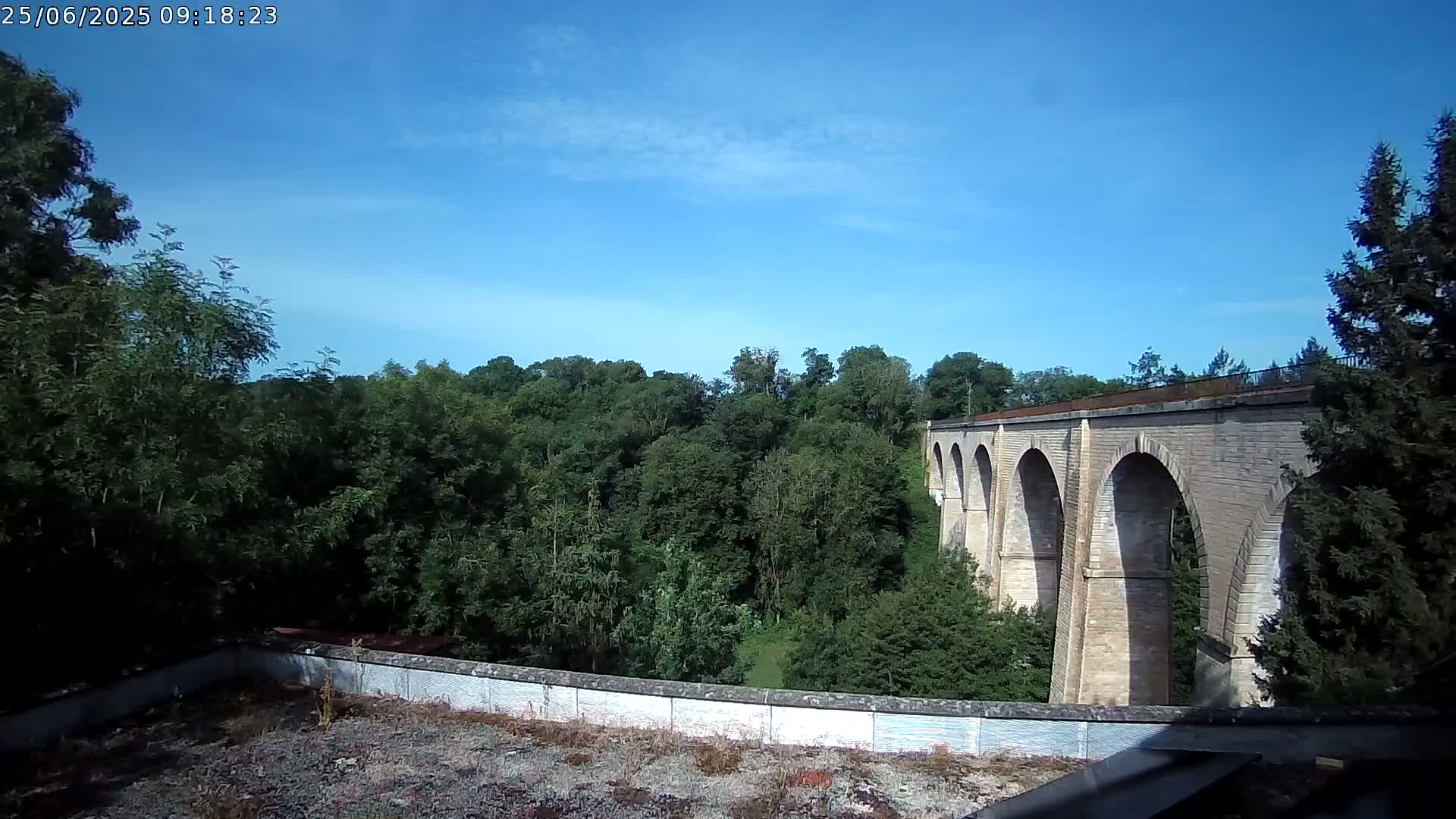 A stone viaduct stretches across a lush green valley under a clear blue sky.