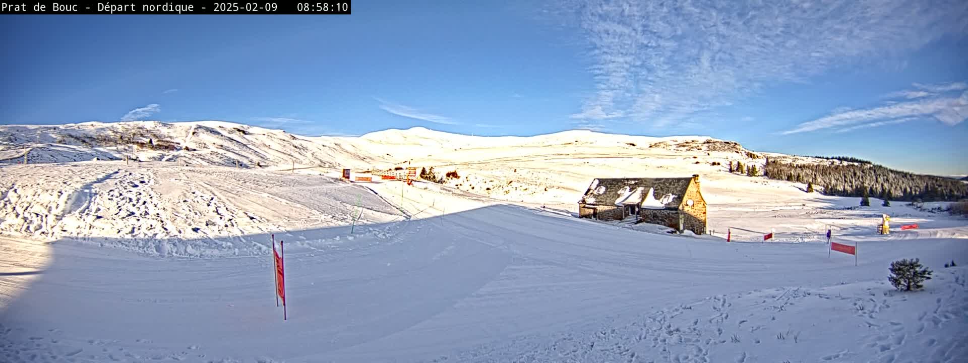 A snow-covered landscape with a small stone building, under a clear blue sky.