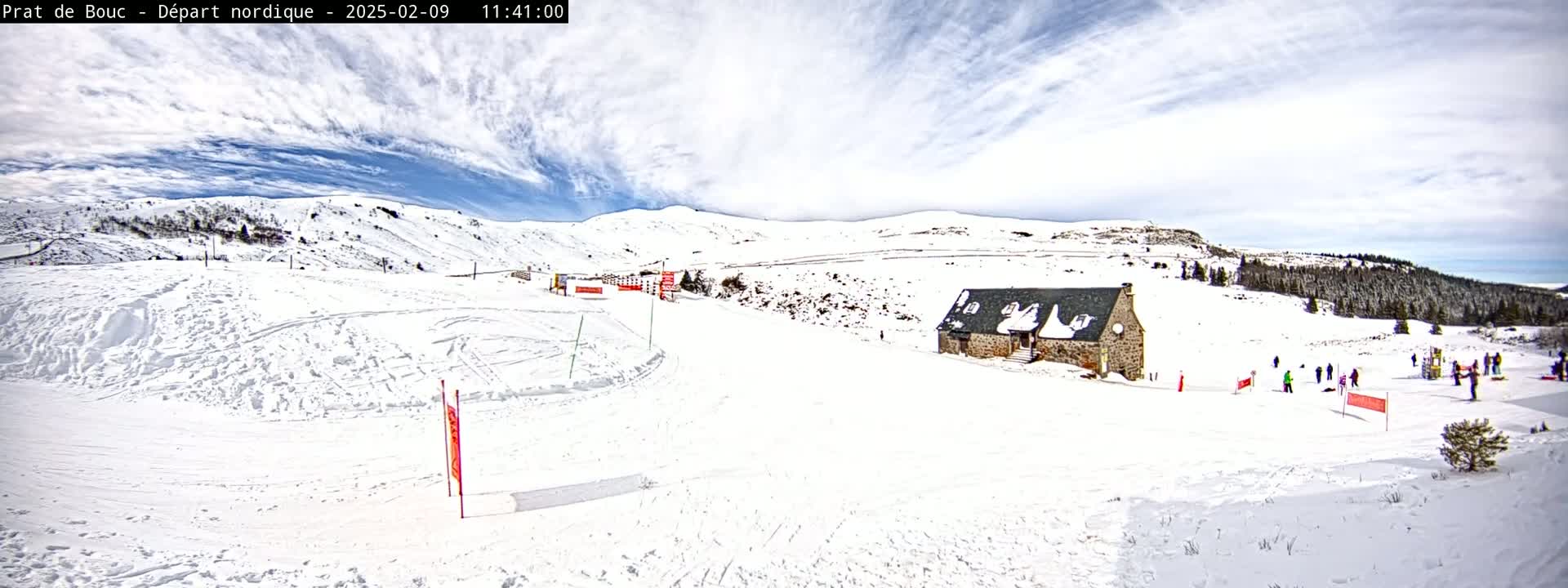 A snow-covered landscape with a stone building and a few people, under a partly cloudy sky.