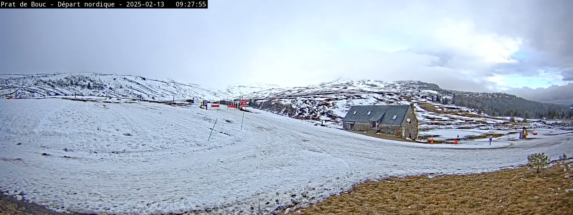 A snow-covered landscape with a stone building and a partly cloudy sky shows a ski area.