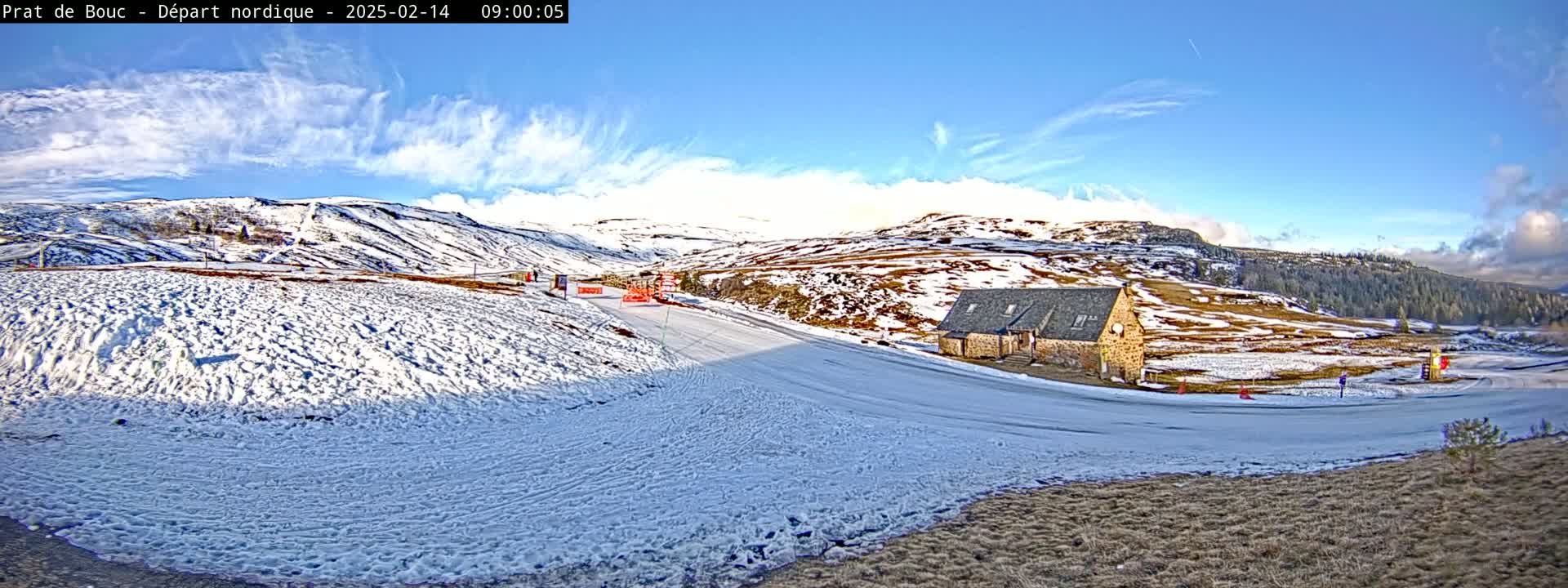 A snow-covered landscape with a stone building and a partly cloudy, bright sky.