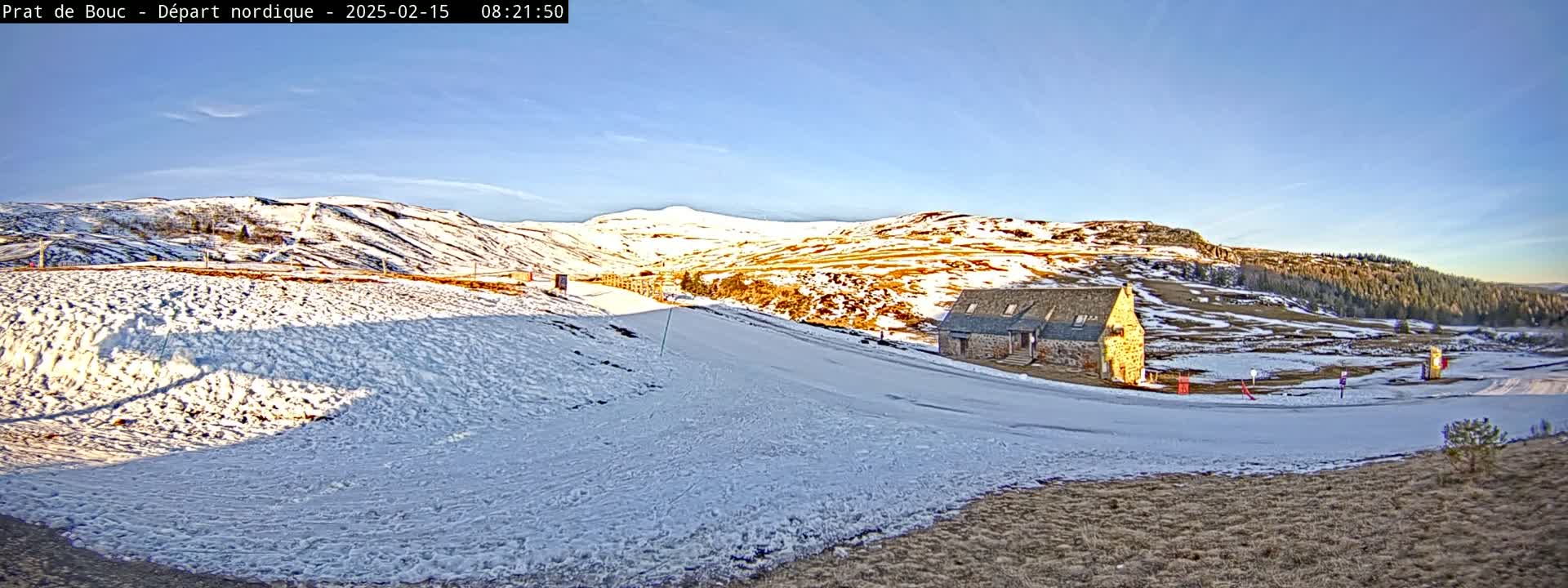 A snow-covered landscape with a stone building and distant hills under a clear blue sky.
