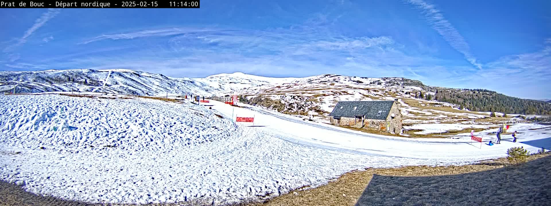 A snow-covered landscape with a stone building and a few people visible under a bright, sunny sky.