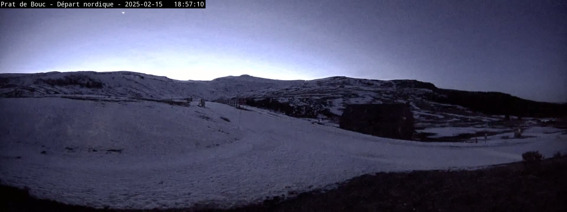 A snow-covered landscape with hills in the background under a twilight sky.